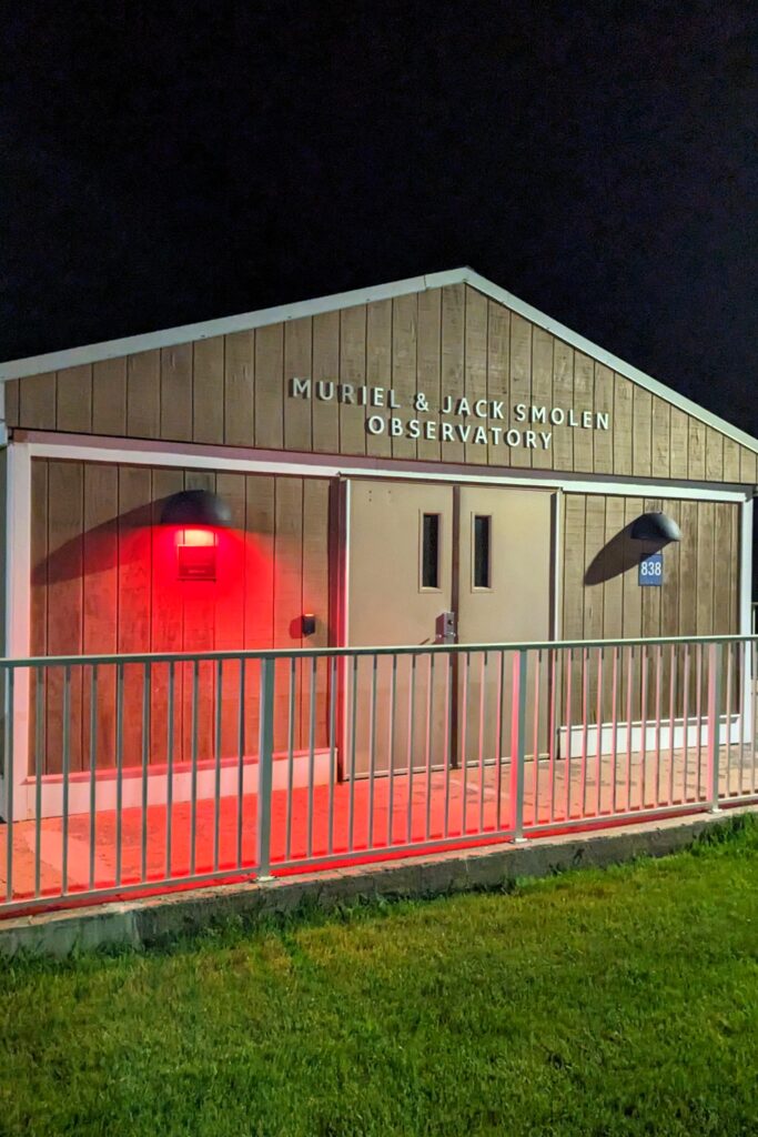 The exterior of the Muriel & Jack Smolen Observatory at night, lit up by a light source out of frame.